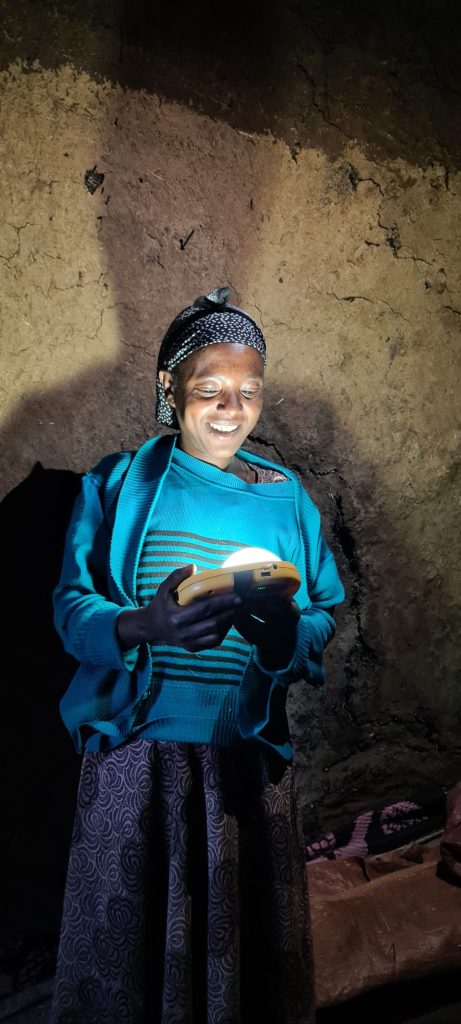 A woman at home in Abuserkema lit by her solar light, holding fresh injera